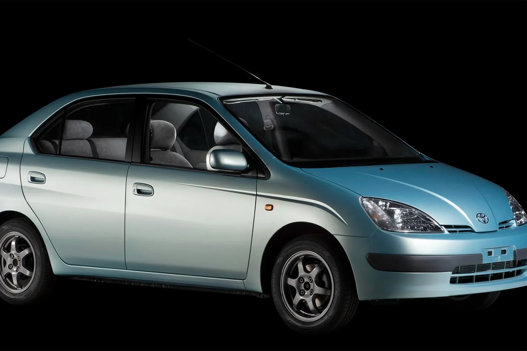 The passenger side of a silver Toyota Prius on a black background.